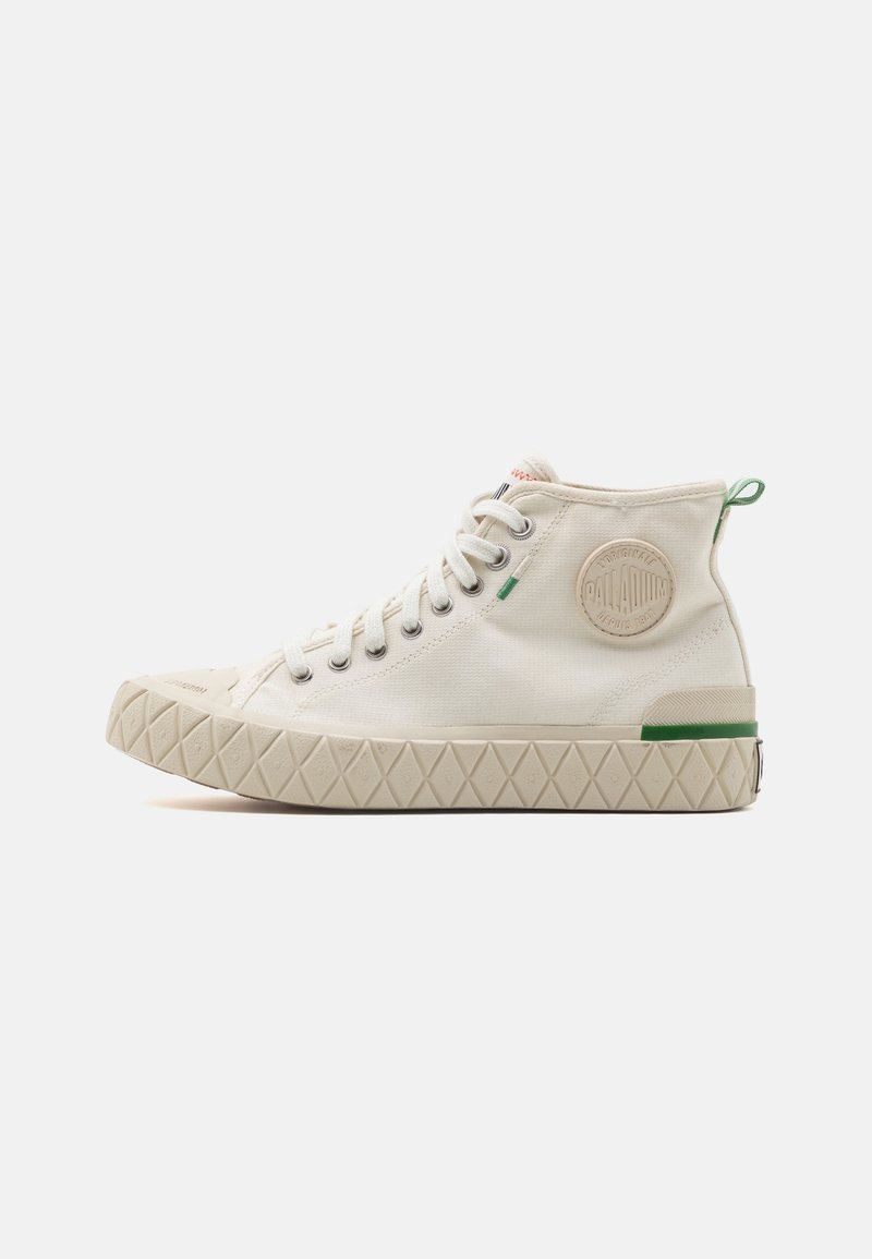 Baskets montantes en toile beige avec lacets blancs, semelle texturée à motif losange, patch rond avec logo sur le côté et détails verts.
