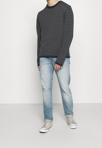 Marinblå stickad tröja med texturerat mönster, rund halsringning och långa ärmar. Ljusblå jeans med rak passform. Grå sneakers med vita sulor.