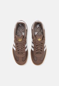 Braune Sneaker mit weißen Streifen und braunen Wildlederakzenten. Schnürdesign, Gummisohle und gemusterte Innensohle mit dem Adidas-Logo.