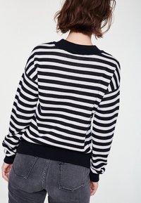 Czarno-biały sweter w paski z prążkowanym kołnierzem i mankietami. Wykonany z miękkiego materiału, ma długie rękawy i luźny krój.