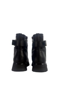 Stivaletti neri in pelle con una cinghia testurizzata e hardware in argento. Presentano un colletto imbottito e una suola in gomma spessa.