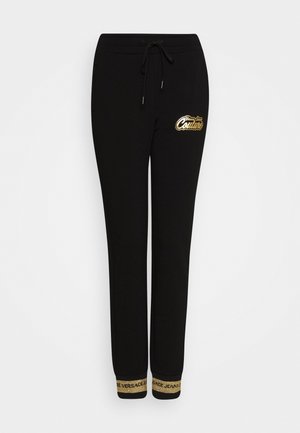 Mustat jogger-housut, joissa on kullanvärinen "Young Couture" -logo reisiosassa ja kullanväriset Versace Jeansin resorit. Kiristysnyörivyötärö.