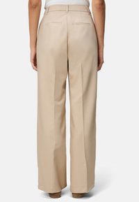 Beige weit geschnittene Hosen mit glatter Textur, ausgestattet mit zwei Gesäßtaschen und einer taillierten Taille. Flacher Schnitt mit scharfen Falten.