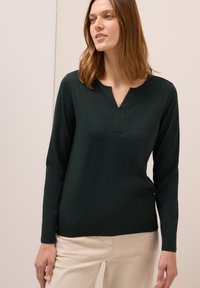 Dunkelgrünes Langarmshirt mit V-Ausschnitt und kleinem Knopfverschluss. Hergestellt aus weichem, dehnbarem Material mit glatter Textur und tailliertem Schnitt.