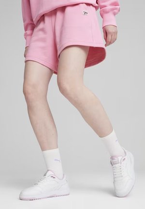 Bermudas de algodón rosa con un corte relajado, combinadas con zapatillas blancas y calcetines con detalles en tonos pastel. Detalle de logo simple en las bermudas.