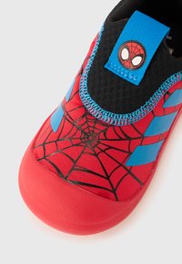 Rød tøysko med blå detaljer og Spider-Man nett-grafikk. Teksturert svart materiale rundt ankelen og en Spider-Man-logo på hempe.