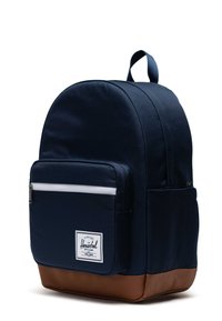 Námornícky modrý batoh s zaobleným tvarom, s bielou zipsovou kapsou a hnedým textúrovaným dnom. Logo nášivka na prednej strane.
