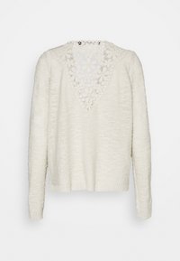 Kremfärgad långärmad tröja med ett texturerat stickmönster. Har en V-formad spetsdetalj på baksidan och ribbade fållar och ärmslut.