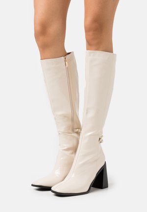 Stivali al ginocchio in pelle verniciata beige con punta quadrata, cerniere laterali e tacco grosso nero. Texture liscia con dettagli in metallo dorato.
