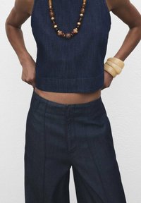Crop top en denim bleu foncé, associé à un pantalon large bleu foncé assorti. Accessoirisé avec un collier en perles en bois et des bracelets volumineux.