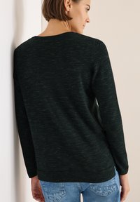 Dunkelgrüner Pullover aus strukturiertem Strickmaterial, mit Rundhalsausschnitt und langen Ärmeln, leicht lässiger Passform und seitlichen Schlitzen.