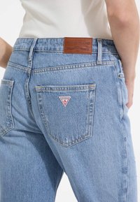 Svetlomodré denimové džínsy s vysokým pásom, s hnedou koženou nášivkou a bielou trojuholníkovou logom na zadnej vrecku.