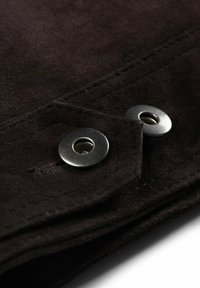 Donkerbruin suède stof met een textuurovervlak, voorzien van zilveren metalen drukkers als accenten nabij de randen, die de nette stikdetails benadrukken.