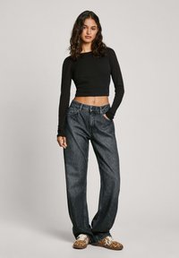 Svart kortärmad långärmad topp i kombination med löst sittande mörk denimjeans. Skorna har ett mönster med leopardtryck. Neutral bakgrund.