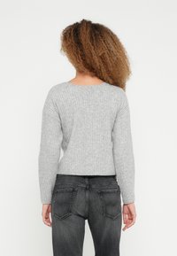 Szary prążkowany sweter z długimi rękawami, okrągłym dekoltem i skróconym dołem, zestawiony z ciemnoszarymi dżinsami z tylnymi kieszeniami i delikatnym efektownym przetarciem.