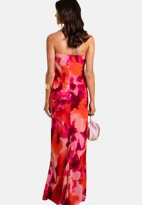 Robe sans manches dans un motif floral vibrant de rose et d'orange, fabriquée en tissu lisse, présentant une silhouette ajustée et un léger traîne.
