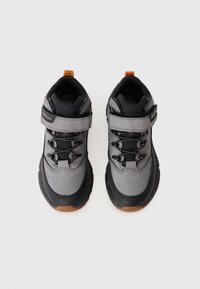 Baskets noires et grises avec une semelle en caoutchouc, un dessus en mesh texturé, des lacets et une sangle en Velcro pour un maintien sécurisé. Tirant orange au talon.