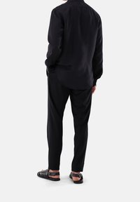 Zwarte longsleeve shirt, relaxte pasvorm, gladde textuur, licht gebogen zoom. Gecombineerd met zwarte op maat gemaakte broek en zwarte sandalen met bandjes.