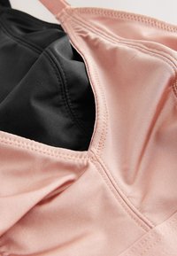 Gros plan d'un soutien-gorge rose doux avec un tissu lisse et des coutures visibles sur une sous-couche noire.