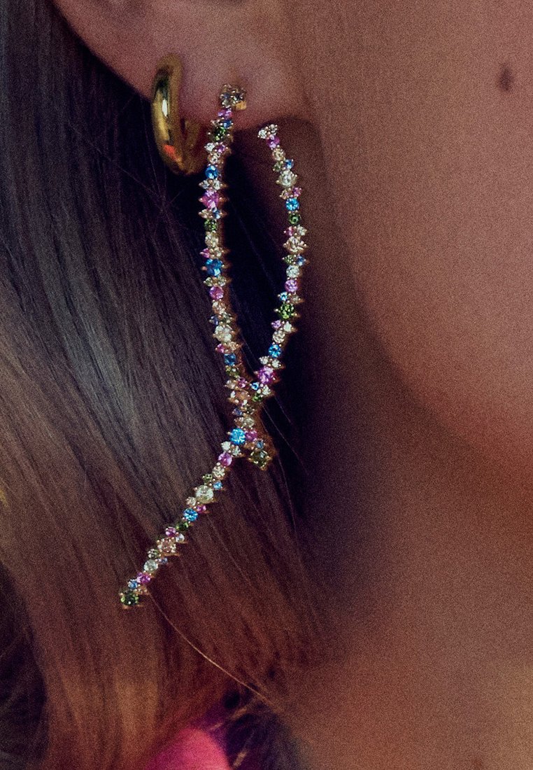 Guldtonade, abstrakt formade örhängen prydda med flerfärgade ädelstenar, med en vriden design och glittriga detaljer.