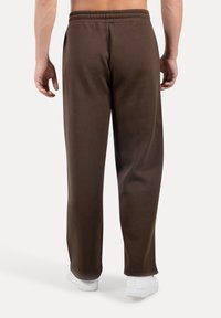 Pantaloni della tuta marroni in cotone con vestibilità comoda, vita elastica e gambe dritte, abbinati a sneakers bianche.