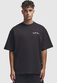 Camiseta negra de gran tamaño hecha de algodón, con mangas cortas, un escote redondo y un pequeño logo blanco en el lado izquierdo del pecho.