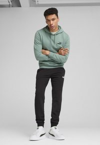 Hoodie vert menthe avec un logo noir, associé à un pantalon de survêtement noir arborant un logo blanc et des baskets blanches avec des accents verts.