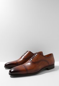 Chaussures habillées en cuir marron avec une finition polie, design à bout droit et cinq œillets pour les lacets. Silhouette élégante et texture lisse.