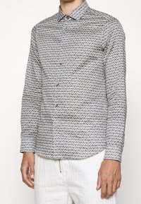 Napapaita, jossa on geometristen mustavalkoisten kuviot, pitkät hihat ja kärjellinen kaulus, valmistettu kevyestä kankaasta.