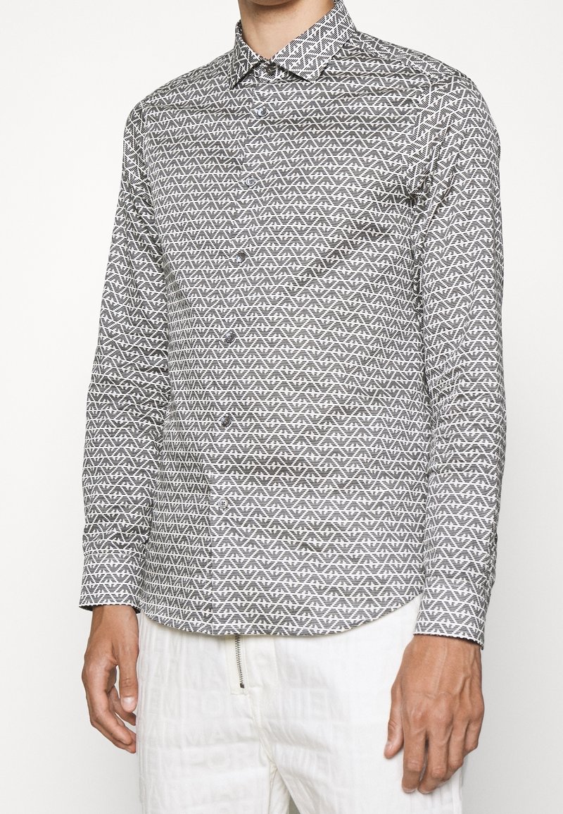 Napapaita, jossa on geometristen mustavalkoisten kuviot, pitkät hihat ja kärjellinen kaulus, valmistettu kevyestä kankaasta.