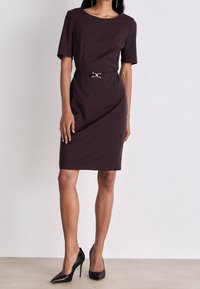 Burgundské pouzdrové šaty s krátkými rukávy, kulatým výstřihem a stříbrným páskem s přezkou. Vyneseno s černými špičatými podpatky.