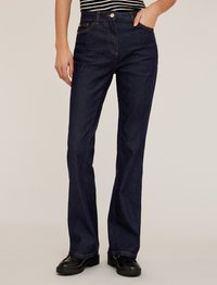 Mörkblå denimjeans med utsvängda ben, dragkedja, fem fickor och orange sömnad. I kombination med en randig topp och svarta platåskor.