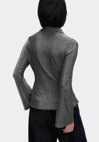 Blank metallisk blazer i sort med lange tætsiddende ærmer og flared manchetter. Skrædderdesignet har krave og syninger på bagsiden.