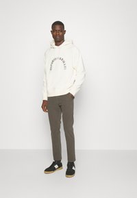 Sweatshirt branco com o logótipo "Emporio Armani", combinado com calças verde-oliva e sapatilhas pretas com detalhes brancos. Textura de tecido suave.