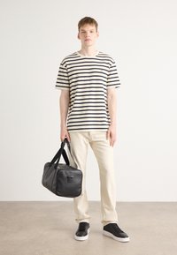 Striped short-sleeve t-shirt in cream and navy, paired with light-colored jeans. Black leather duffel bag with short handles and simple hardware.