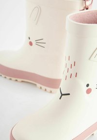 Bottes de pluie en caoutchouc blanches avec des semelles roses, présentant un design de visage de lapin avec des moustaches, un nez et des accents d'oreilles. Doublure intérieure texturée.