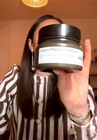 Person iført stribet skjorte holder en krukke mærket "Absolut Repair Molecular" tæt på kameraet og skjuler delvist deres ansigt.