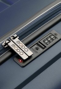 Valigia rigida blu con superficie testurizzata, dotata di doppie cerniere metalliche, serratura a combinazione integrata e foro per chiave approvato TSA.