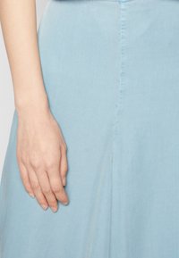Vestido azul claro com uma textura suave e ligeiramente macia. A saia escoa suavemente a partir da cintura, com um detalhe de costura central visível.