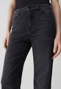 Jeans en denim noir taille haute avec une jambe droite. Comprend des poches avant, une fermeture à bouton et à zip, et un léger délavage sur le tissu.