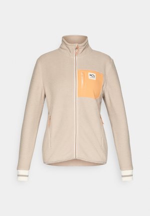 Chaqueta de forro polar beige con cuello alto, cierre con cremallera en el frontal, bolsillo en el pecho naranja, dos bolsillos laterales y puños a rayas. Textura suave, diseño casual.