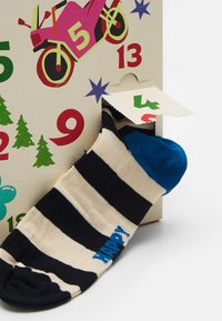 Stripede sokker i marineblå og cremefarvet med en blå hæl og tå. Har teksten "HAPPY" i blåt. Delvist synlig i en adventskalenderåbning.