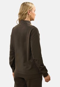 Felpa marrone con colletto alto, caratterizzata da una vestibilità comoda e polsini a costine. Il tessuto appare morbido con una texture liscia.