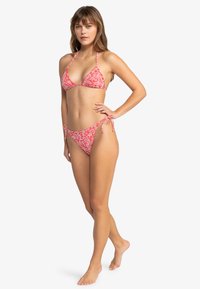 Červený kvetinový bikini s trojuholníkovým vrchom a plavkami na viazanie na bokoch. Obsahuje malý kvetinový vzor, nastaviteľné popruhy a mäkkú textúru látky.