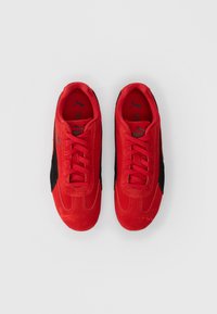 Ζευγάρι κόκκινων και μαύρων αθλητικών παπουτσιών Puma με κορδόνια, από πάνω σε λευκό φόντο.