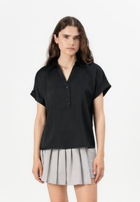 Kortermet svart bluse med krage, knappelukking foran og en avslappet passform. Stoffet ser glatt ut; har rullede ermer og et enkelt design.