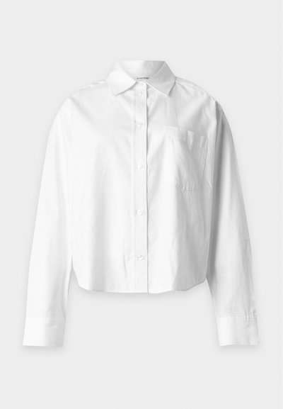 Chemise blanche à manches longues avec boutons, col pointu et poche poitrine, présentée sur un fond clair uni.