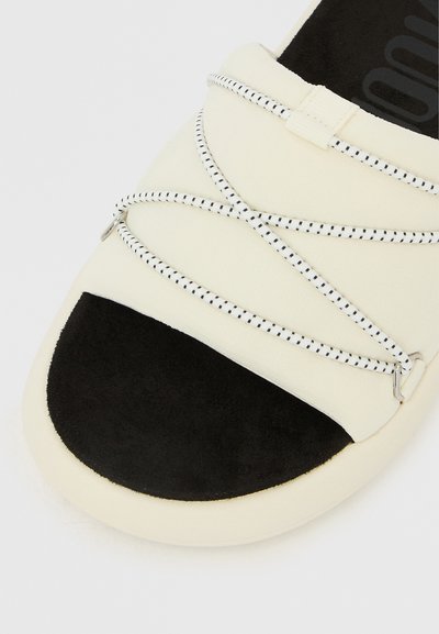 Κοντινή λήψη υποδημάτων με κοντινό επάνω μέρος σε ανοιχτό μπεζ χρώμα, μαύρο προστατευτικό στη μύτη και λευκά ελαστικά κορδόνια τυλιγμένα μπροστά.