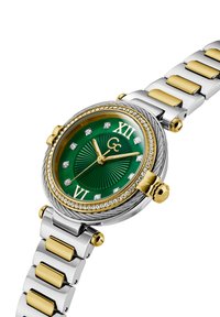 Roheline ümmargune kell kuldsete aktsentidega, mineraalglasuur, teemantmarkerid ja kahevärviline randmevärv, mis koosneb hõbedast ja kuldsetest linkidest.