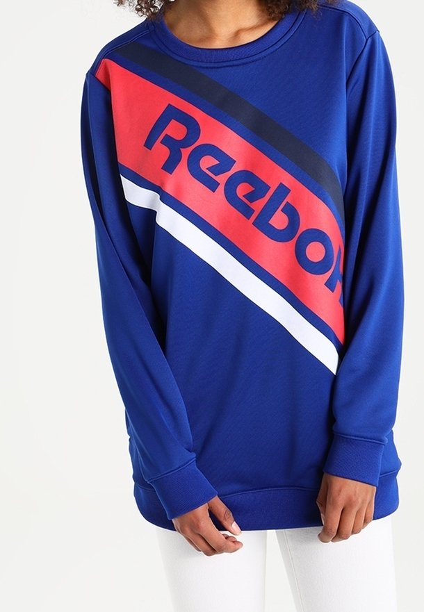 Kungablå sweatshirt med ett diagonalt röd streck och vita och svarta accenter. Stort "Reebok"-logotyp iögonfallande placerad.